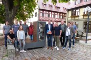 Rund ein Dutzend Gemeinderatsmitglieder am neuen Bücherschrank mit Bank vor dem Rathaus in Grettstadt.