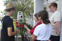 Ein Mitarbeiter des Amtes für Ländliche Entwicklung Unterfranken leitet zwei Schülerinnen und einen Schüler an, ein digitales Messgerät zu bedienen.